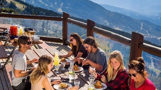 Guests eating at a long table on a mountain deck above the Whistler valley